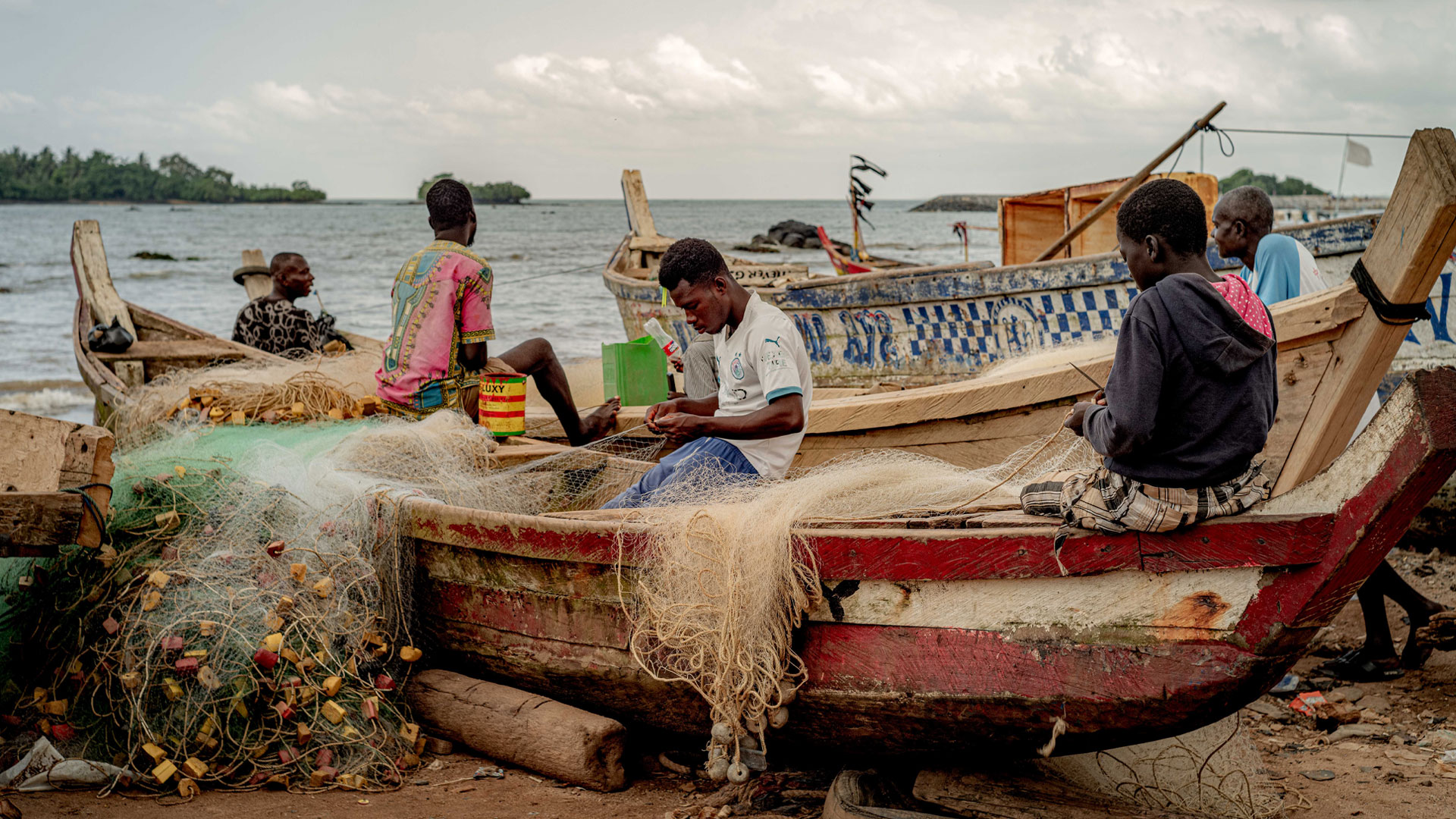 Group of young fishermen sitting in a boat at shore with fishnets