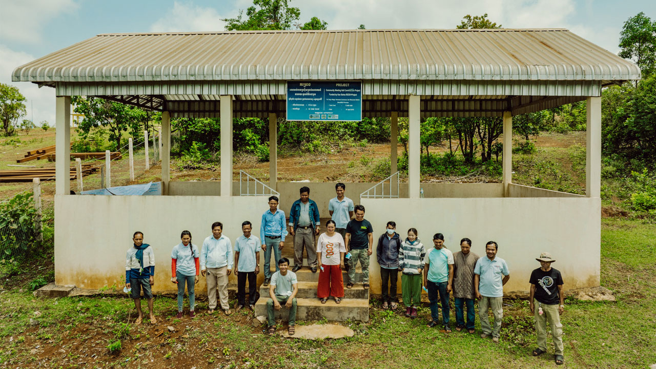 A group of community members stands in front of local infrastructure development supported by REDD+ funding