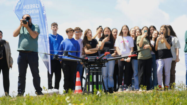 A group of youth standing in a field watch a drone prepare to take off