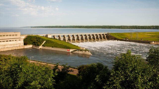 A dam with green landscape around it and a blue sky in the background