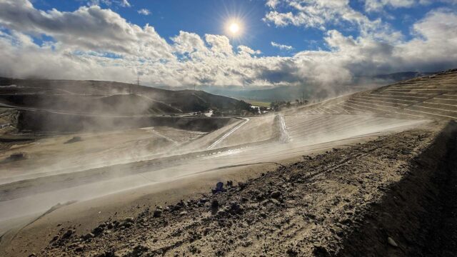 View of a landfill with a blue sky, clouds, and shining sun in the background