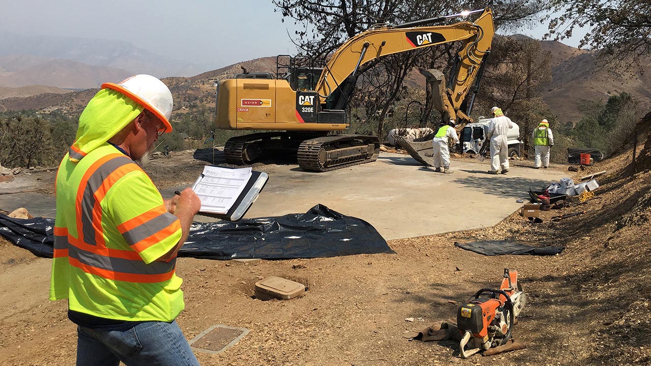 Tetra Tech employee jots down information on a pad as other workers clear disaster debris