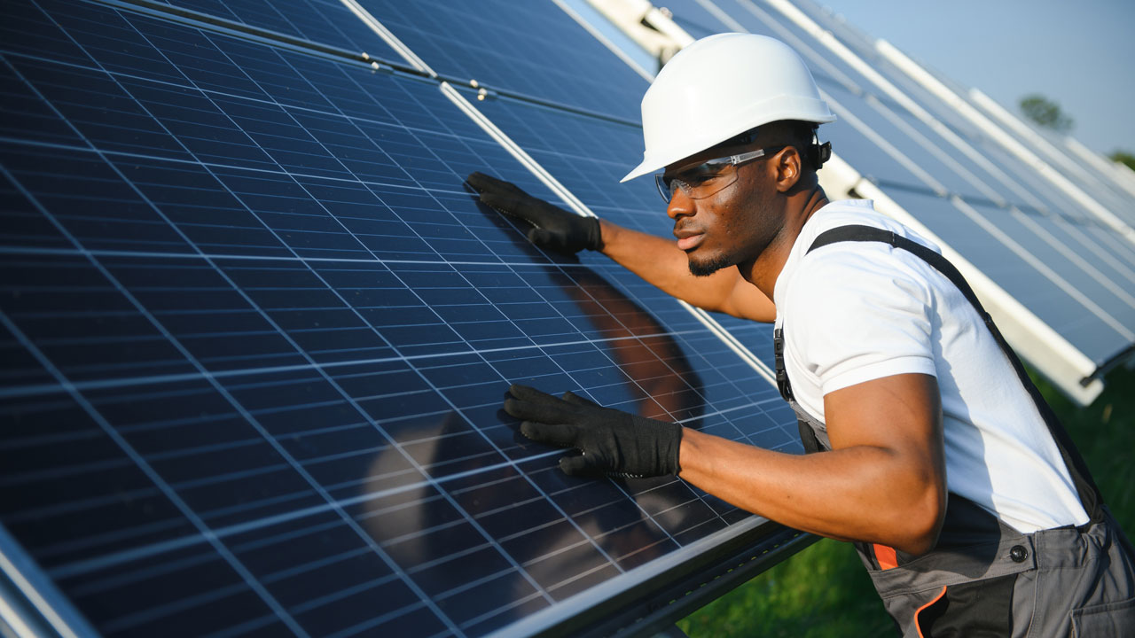 An engineer wearing protective equipment while placing hands on solar panels