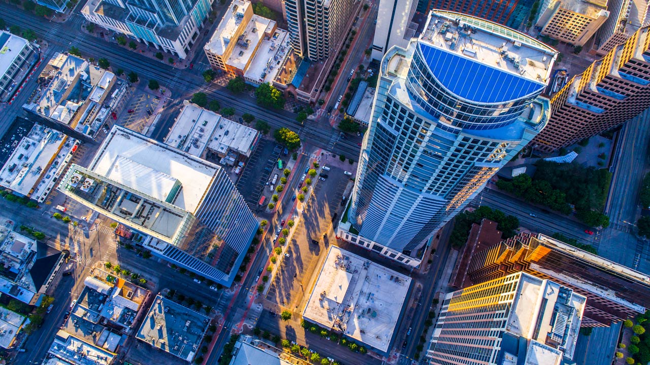 An aerial view of an urban area showing the tops of high rise, and low rise builds, streets, and vegetation