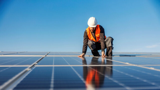 An engineer wearing safety equipment installing solar panels on a roof